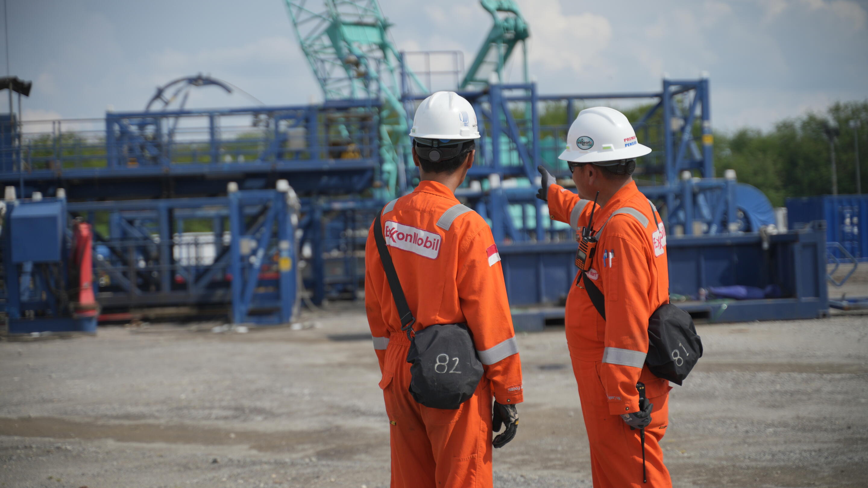 Employees in Indonesia in hard hats pointing and looking at equipment