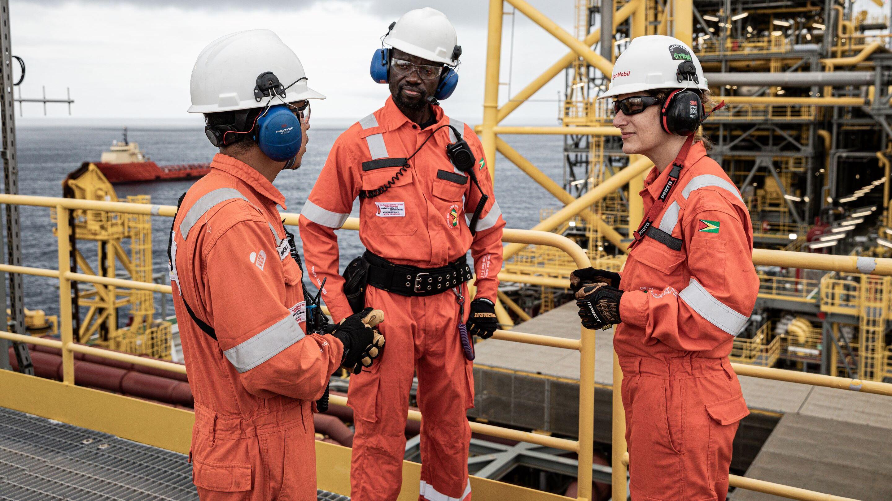 Three employees in hard hats talking on a vessel with the ocean in the background