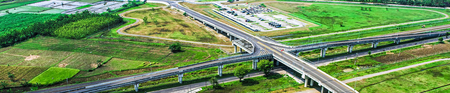Aerial view of a curved highway interchange surrounded by green fields and farmlands, with a decorative green landscaped area in the center of the loop.