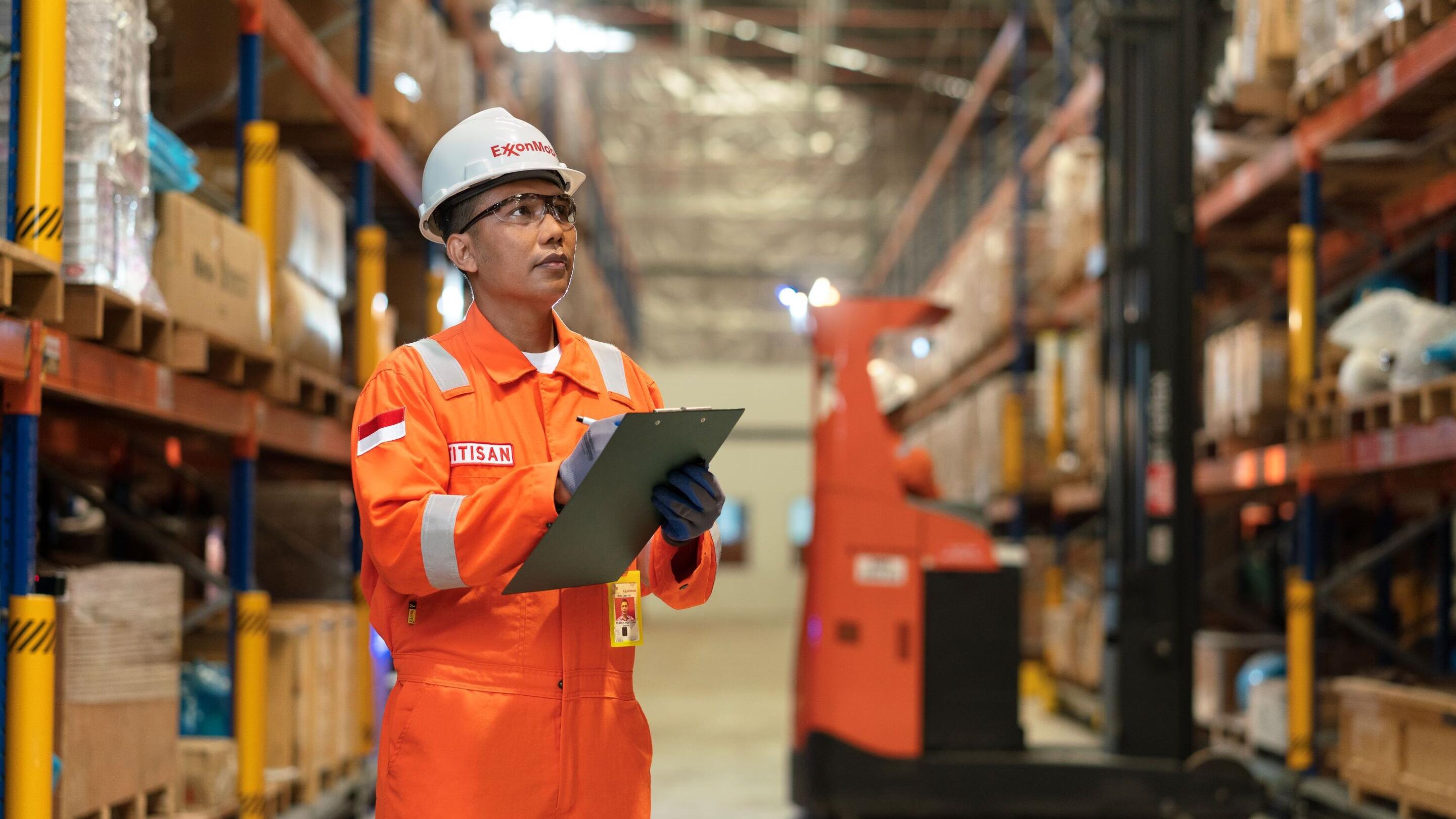 A person in an orange safety jumpsuit and a white hard hat labeled 