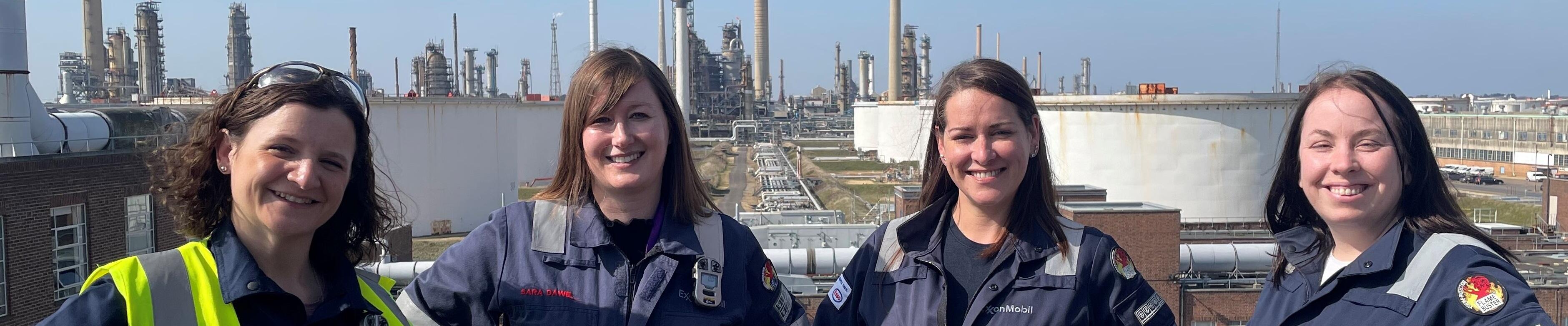 four women employees in protective gear with refinery backdrop