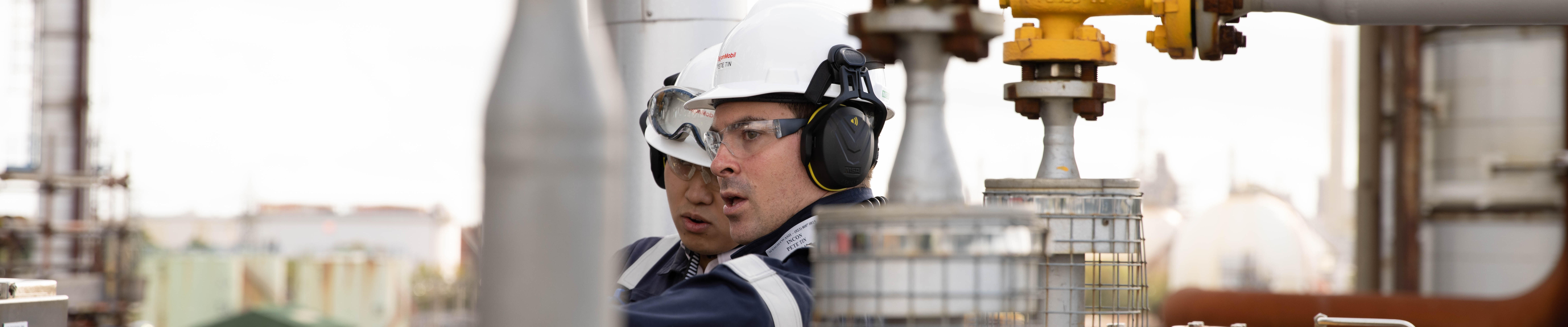 refinery workers in protective gear around pipes and valves
