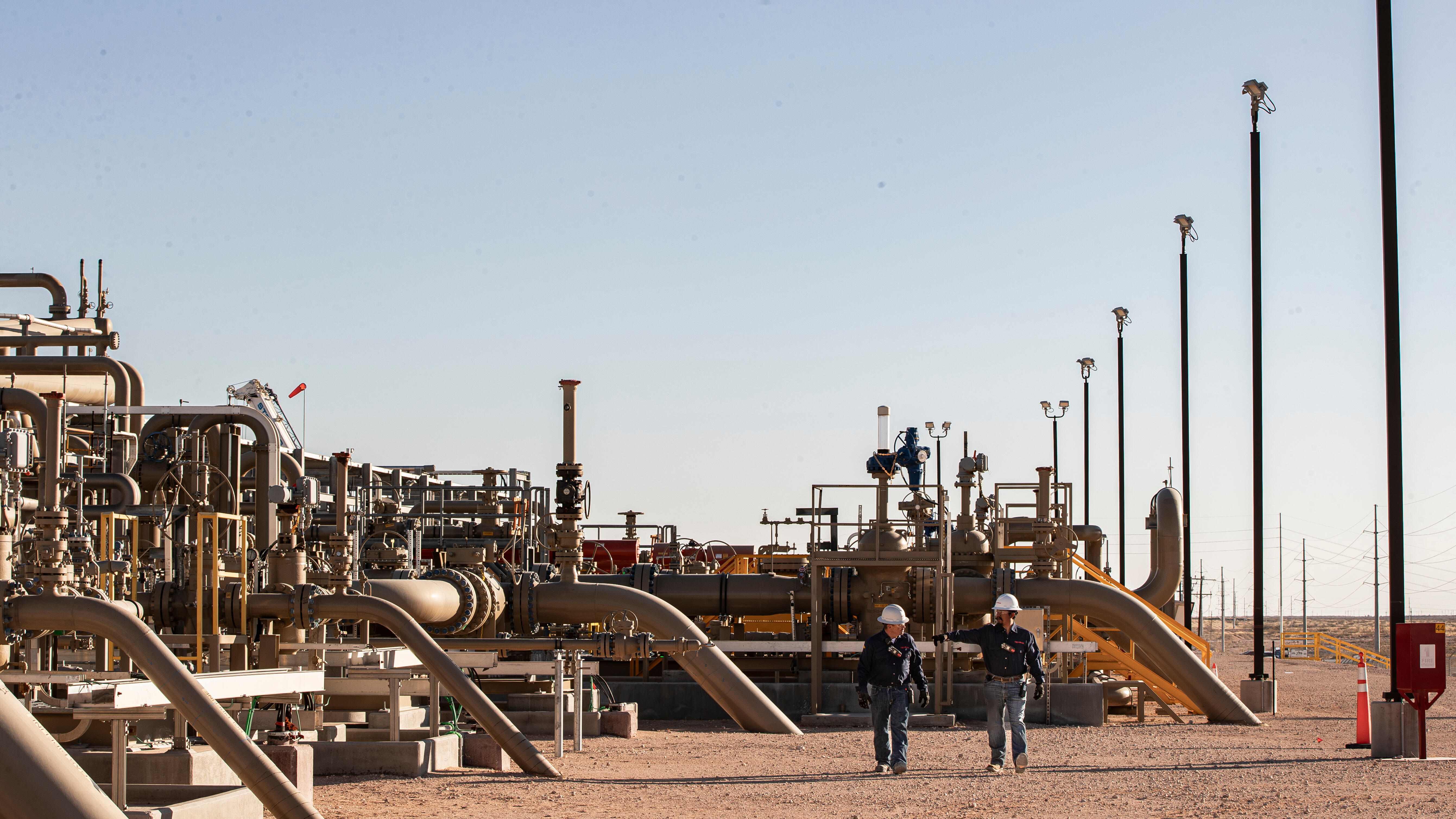 two people walking through large pipes and pipelines at facility in arid area