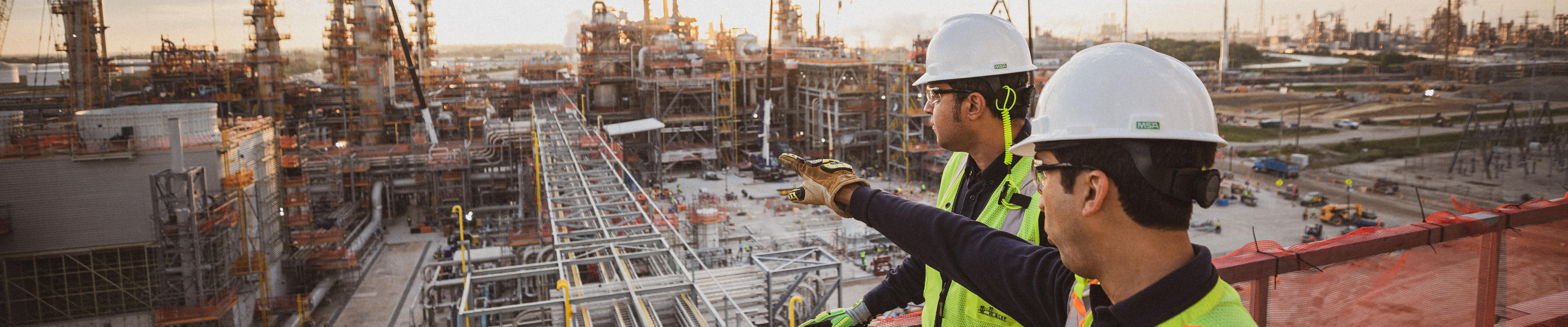 two workers standing on elevated platform overlooking construction at petrochemical facility