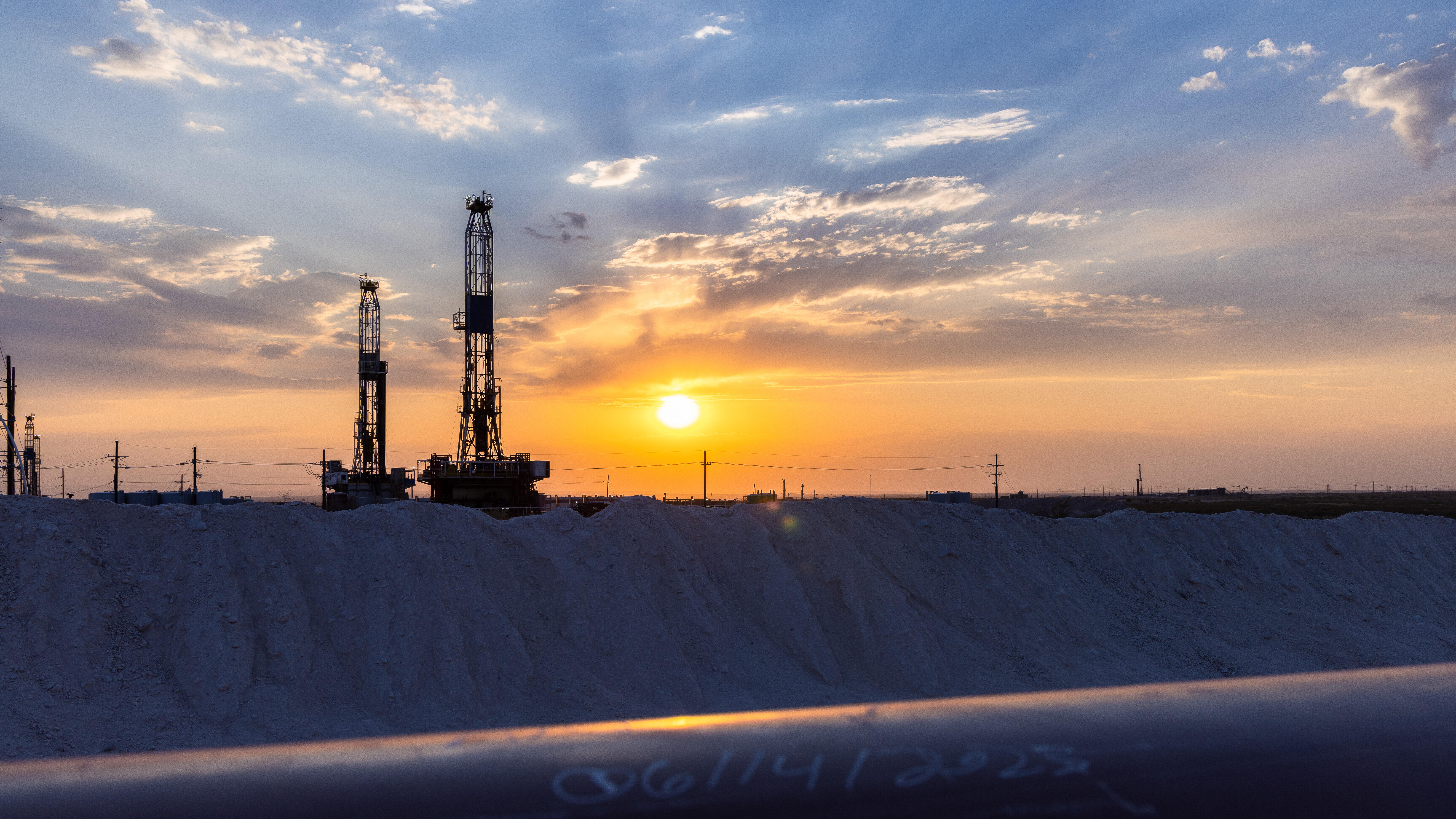 oil drill rigs at sunset with a pipeline in foreground
