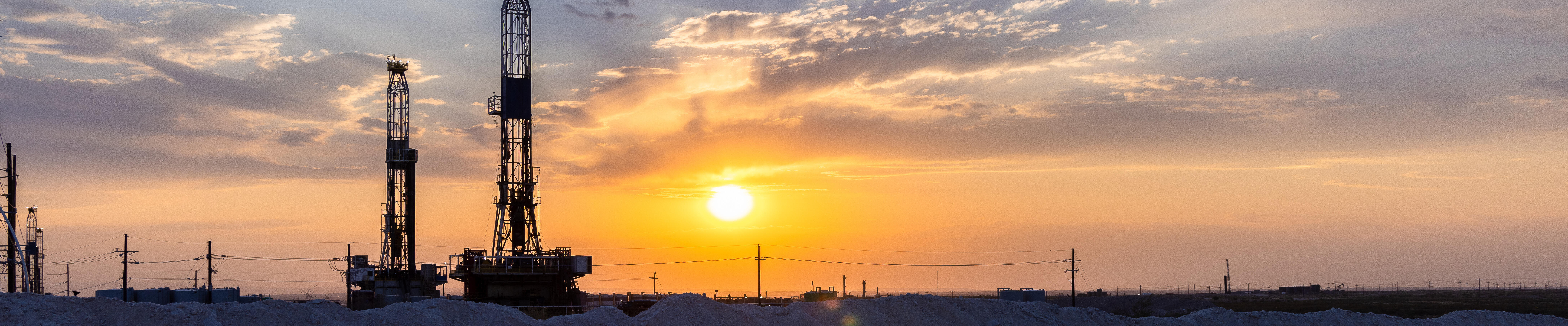 oil drill rigs at sunset with a pipeline in foreground